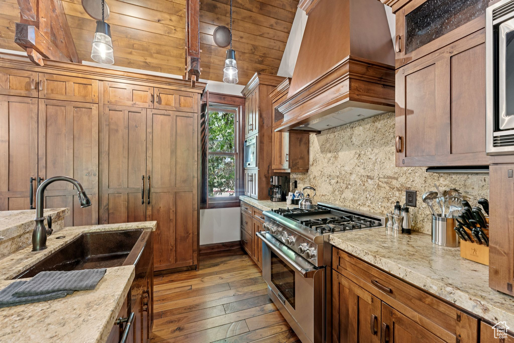 Kitchen with stainless steel stove, custom range hood, decorative backsplash, light wood-type flooring, and brown cabinetry