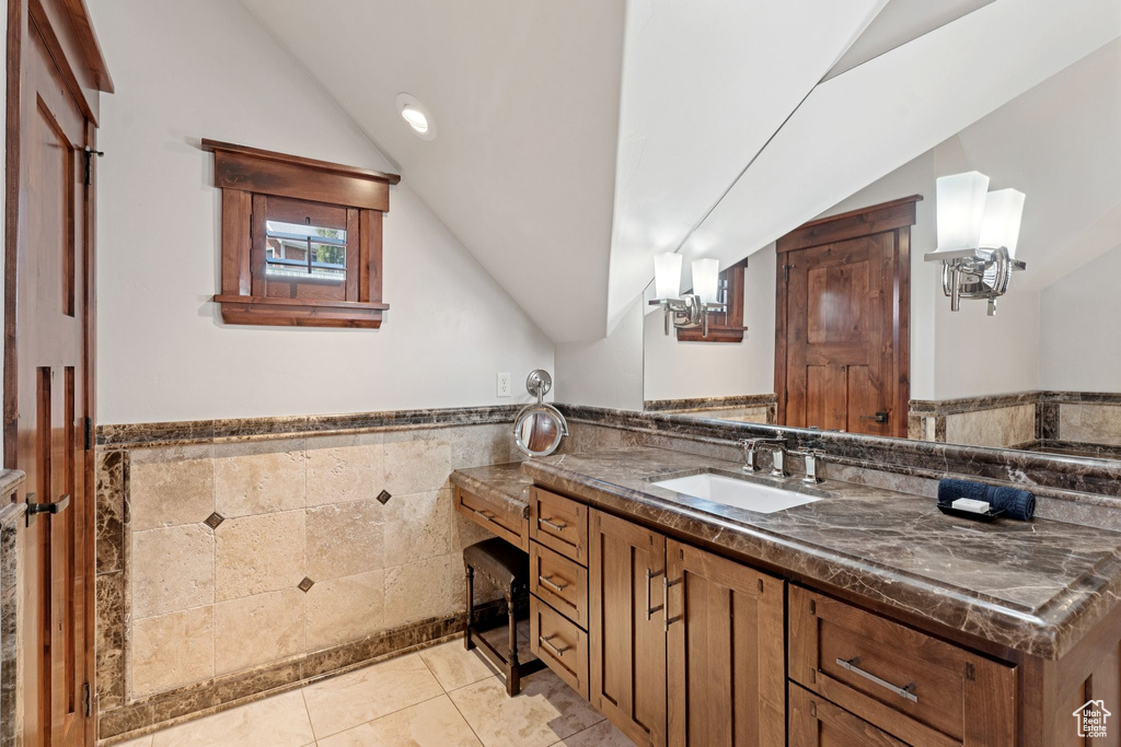 Bathroom featuring vaulted ceiling, tile walls, vanity, tile patterned floors, and wainscoting