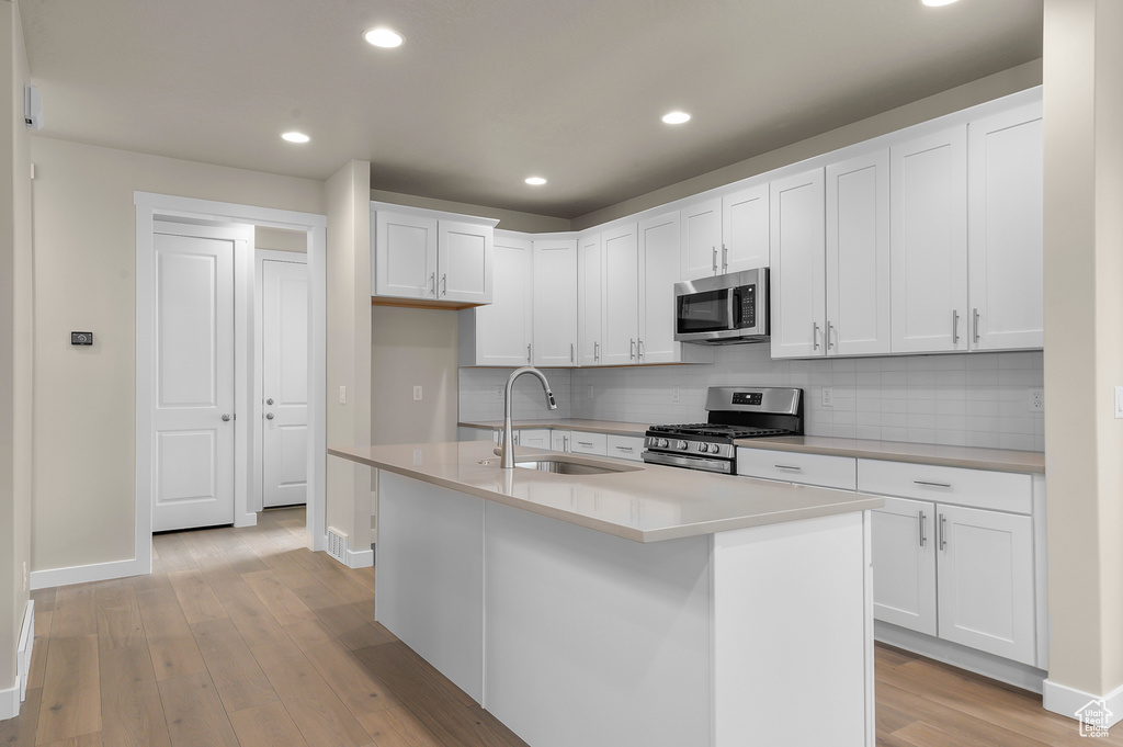 Kitchen featuring appliances with stainless steel finishes, tasteful backsplash, light wood-style flooring, white cabinetry, and recessed lighting