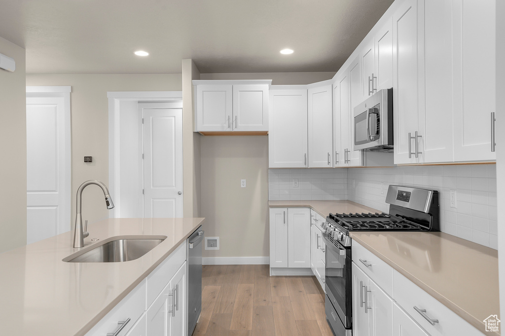 Kitchen with appliances with stainless steel finishes, light wood finished floors, recessed lighting, white cabinetry, and backsplash
