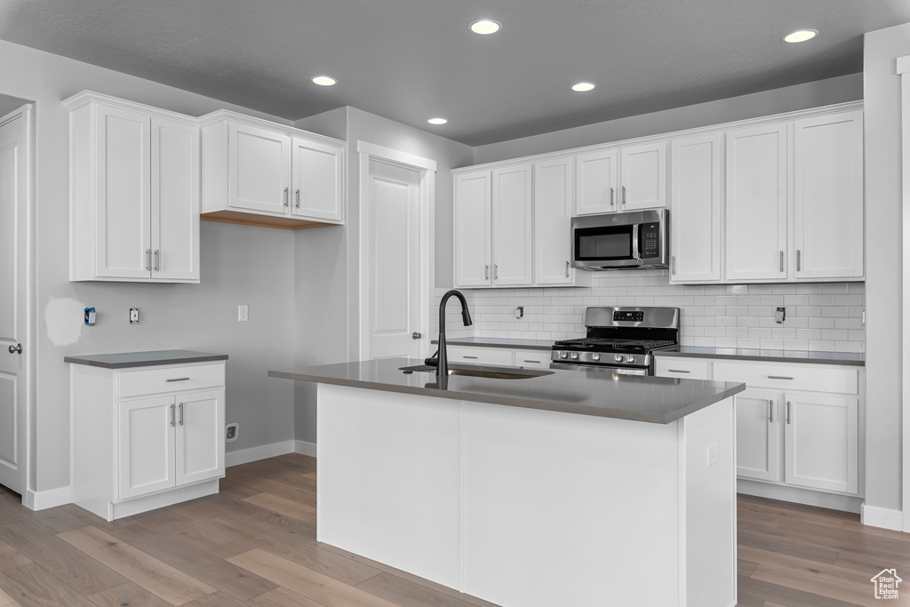 Kitchen featuring appliances with stainless steel finishes, dark countertops, light wood-style flooring, white cabinetry, and recessed lighting