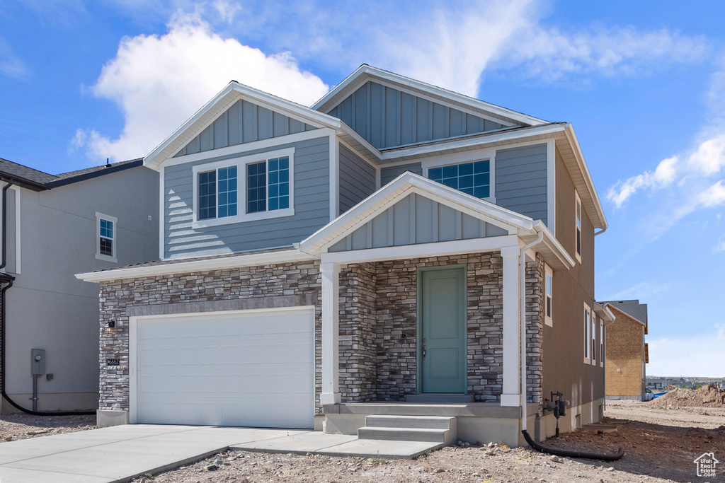 View of front of home featuring board and batten siding, a garage, stone siding, and driveway