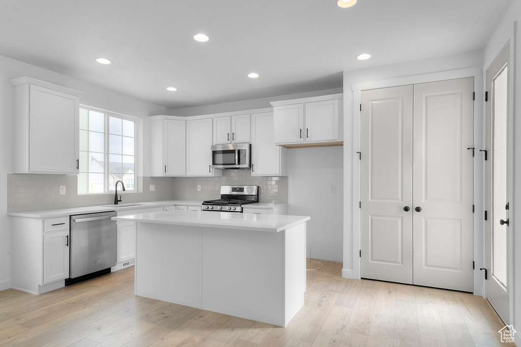 Kitchen with stainless steel appliances, light countertops, white cabinets, decorative backsplash, and recessed lighting
