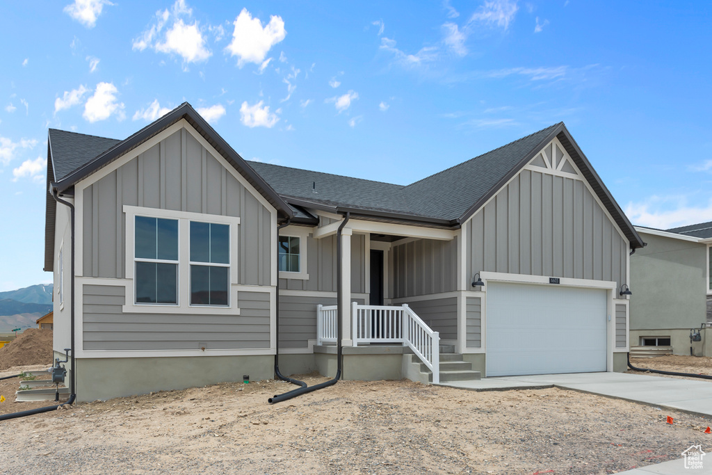 View of front of property featuring board and batten siding, an attached garage, driveway, and a shingled roof