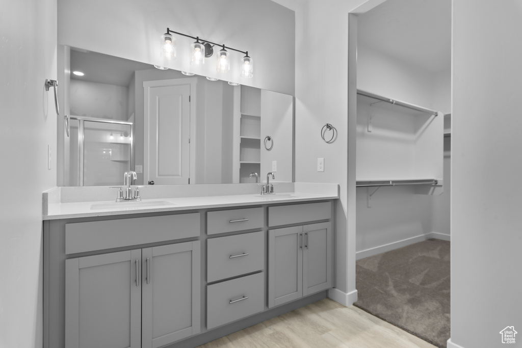 Full bathroom featuring double vanity, a shower stall, a spacious closet, and wood finished floors
