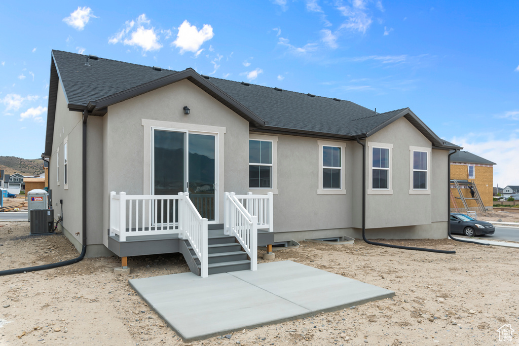 Back of property with stucco siding, roof with shingles, and a patio