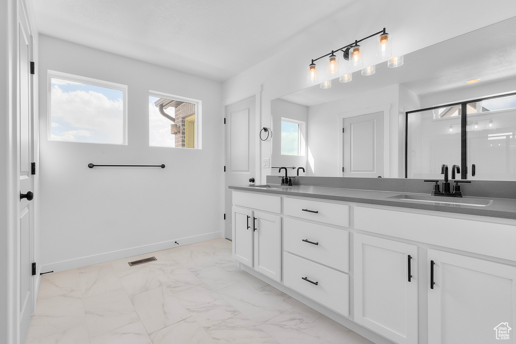 Full bathroom with double vanity, marble look tiles, and a shower stall