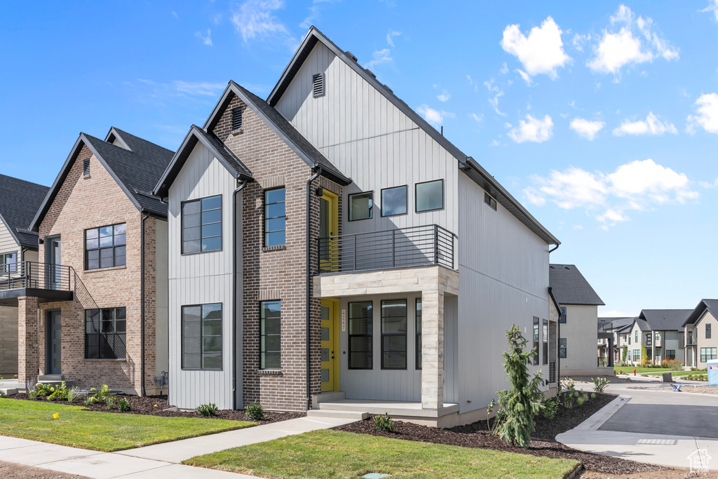 View of front of property featuring board and batten siding, a residential view, a front lawn, and a balcony