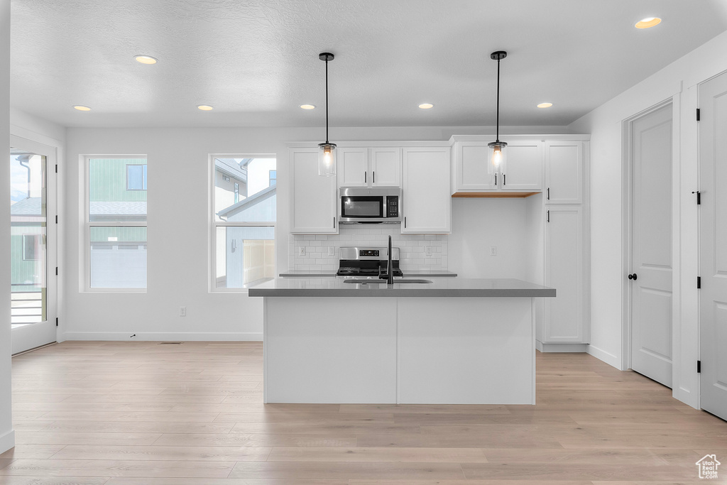 Kitchen with appliances with stainless steel finishes, white cabinetry, light wood finished floors, decorative backsplash, and recessed lighting