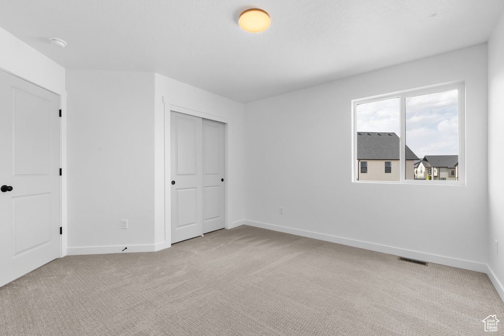 Unfurnished bedroom with light carpet and a closet
