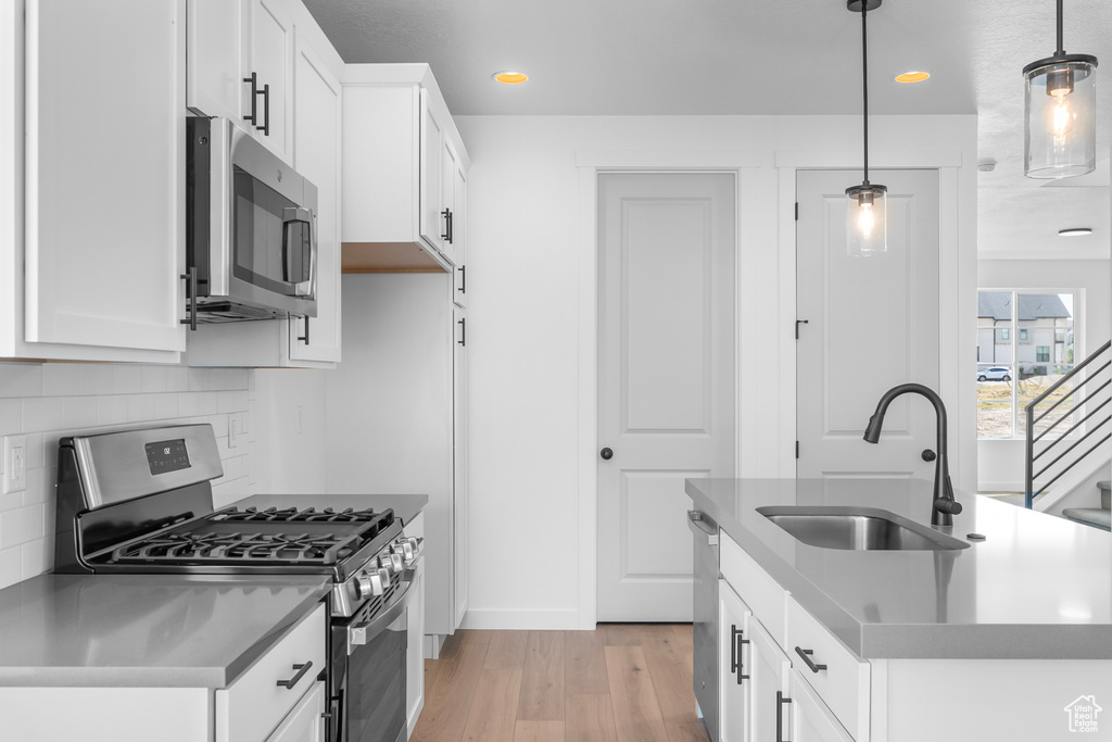 Kitchen with stainless steel appliances, light wood-style floors, tasteful backsplash, recessed lighting, and white cabinets