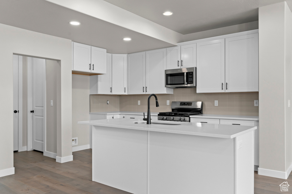 Kitchen featuring appliances with stainless steel finishes, tasteful backsplash, wood finished floors, light countertops, and recessed lighting