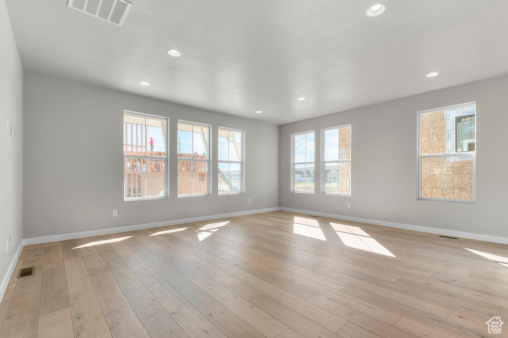 Empty room with healthy amount of natural light, light wood finished floors, and recessed lighting