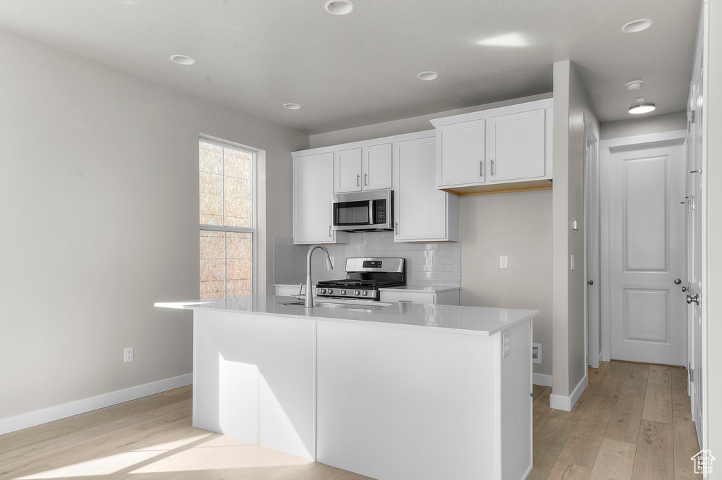 Kitchen with appliances with stainless steel finishes, light wood-style flooring, white cabinetry, backsplash, and recessed lighting
