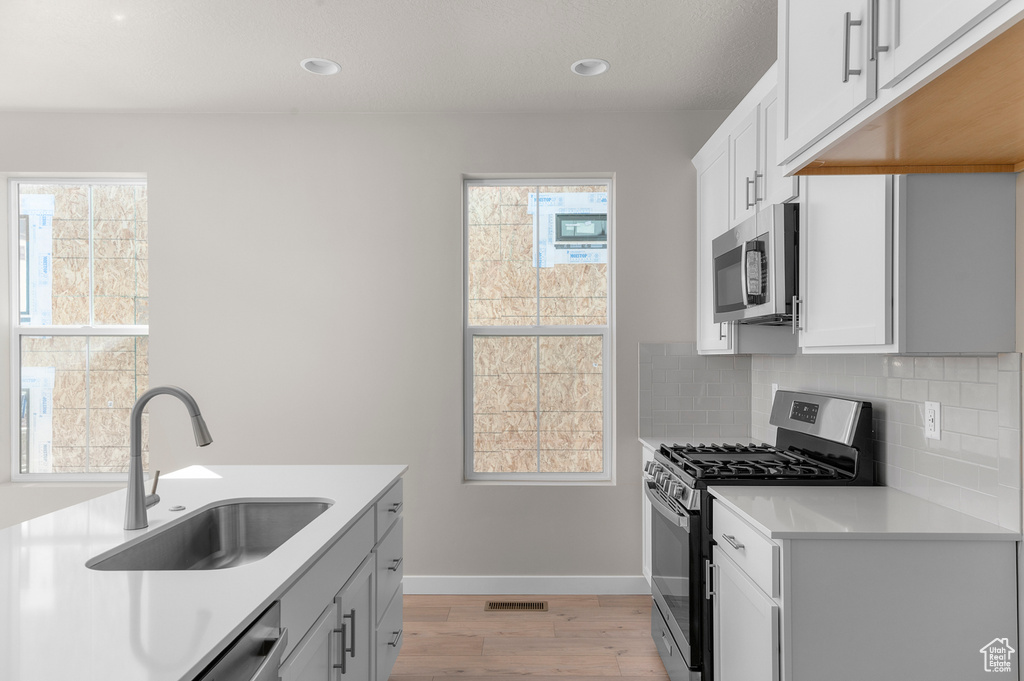 Kitchen featuring appliances with stainless steel finishes, light wood-type flooring, backsplash, light countertops, and plenty of natural light