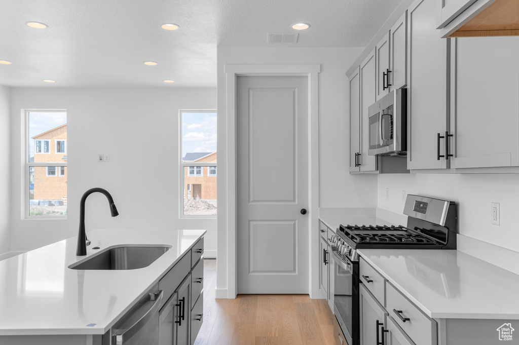 Kitchen with stainless steel appliances, recessed lighting, light wood-style floors, light countertops, and a center island with sink