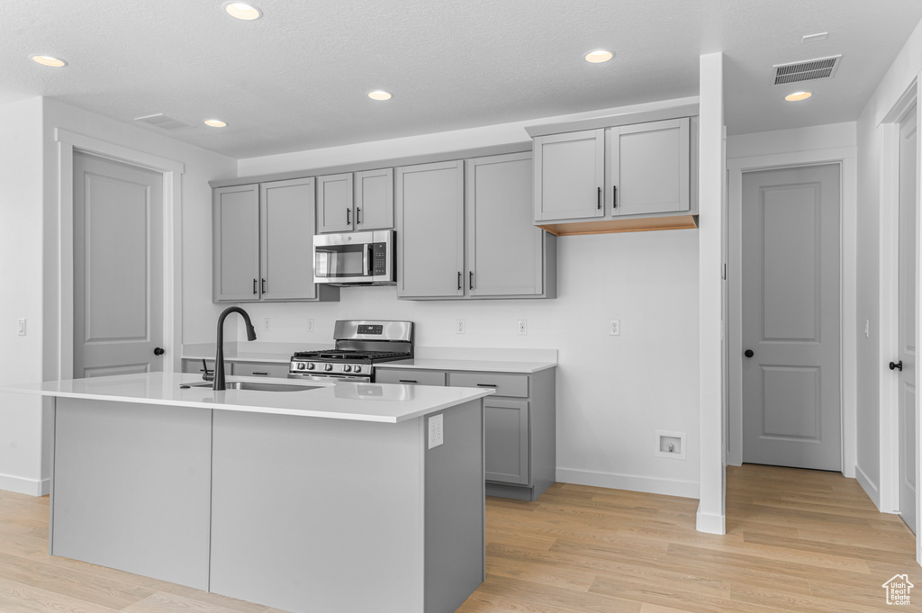 Kitchen featuring stainless steel appliances, gray cabinetry, light wood finished floors, a kitchen island with sink, and recessed lighting