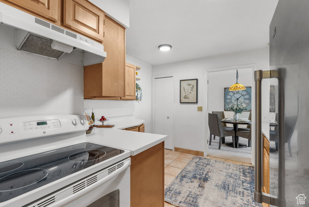 Kitchen featuring electric range, under cabinet range hood, light countertops, and light tile patterned floors