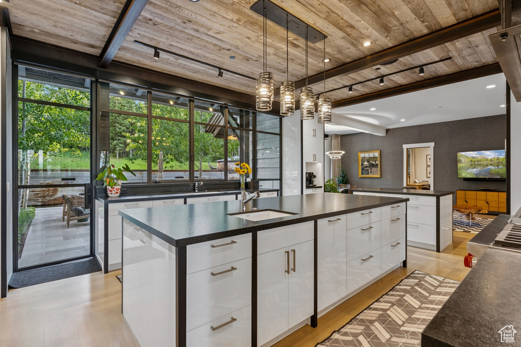 Kitchen with dark countertops, wood ceiling, modern cabinets, white cabinetry, and a kitchen island with sink