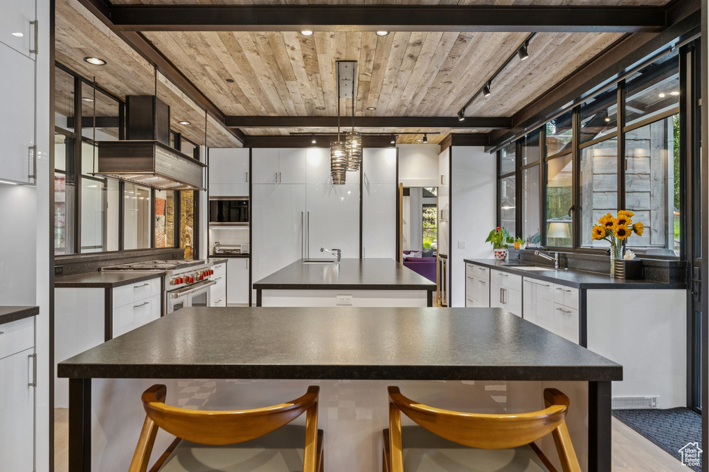 Kitchen with dark countertops, high end stainless steel range oven, a wooden ceiling with exposed beams, and a kitchen island with sink