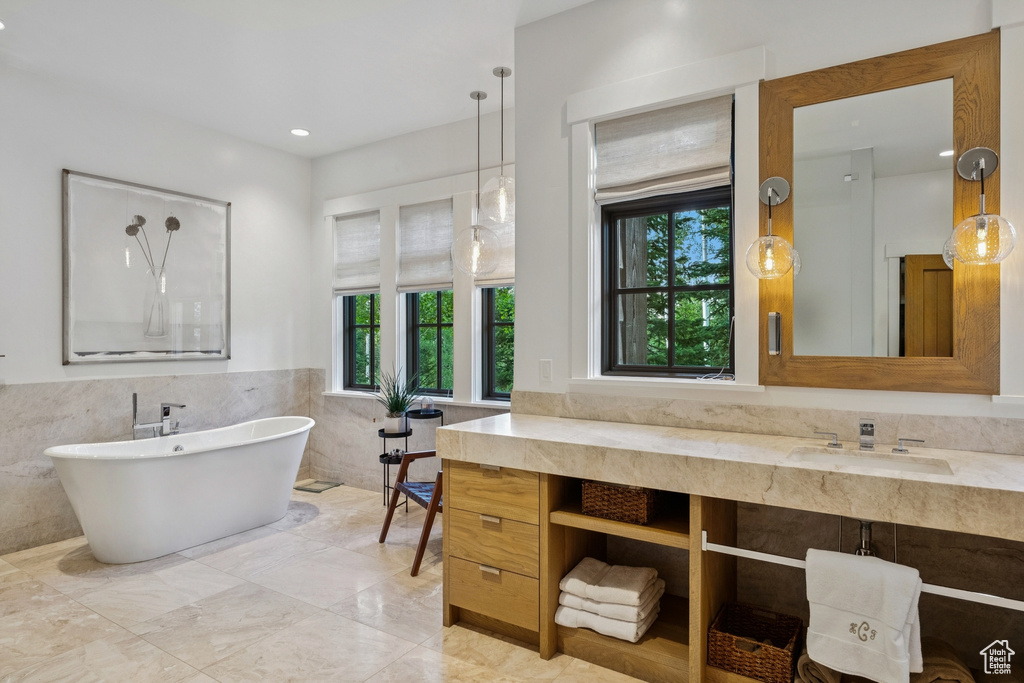 Bathroom featuring tile walls, a soaking tub, vanity, wainscoting, and marble finish flooring