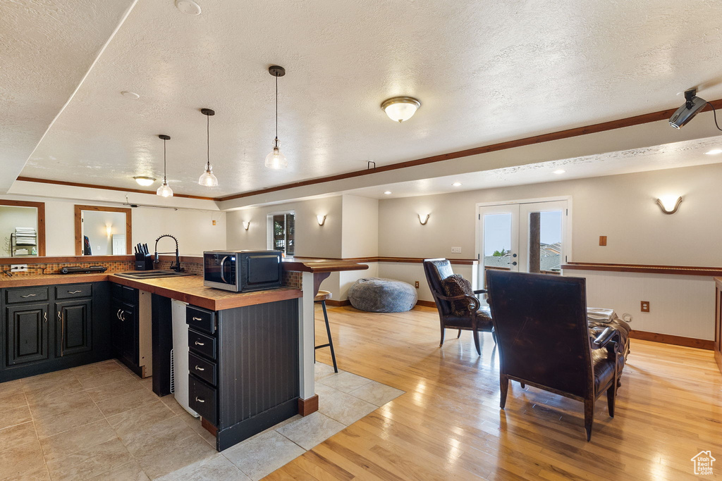 Kitchen featuring black microwave, wooden counters, a breakfast bar, a textured ceiling, and light wood-type flooring
