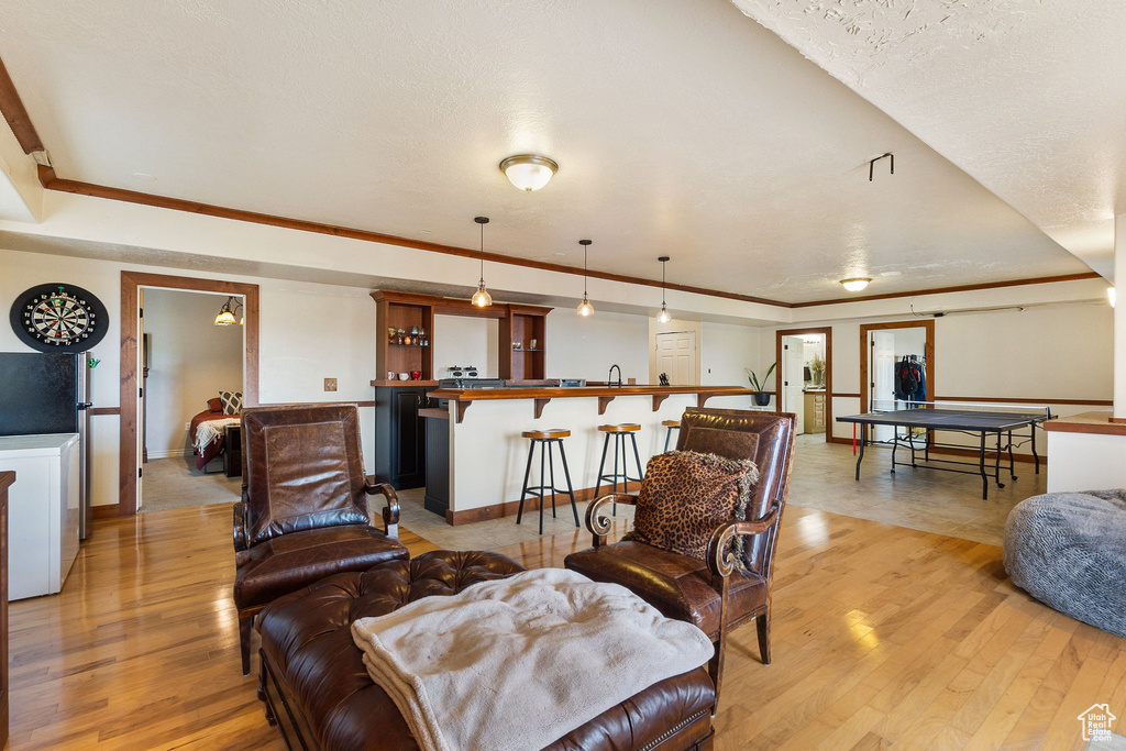 Living area featuring light wood finished floors, crown molding, and bar area