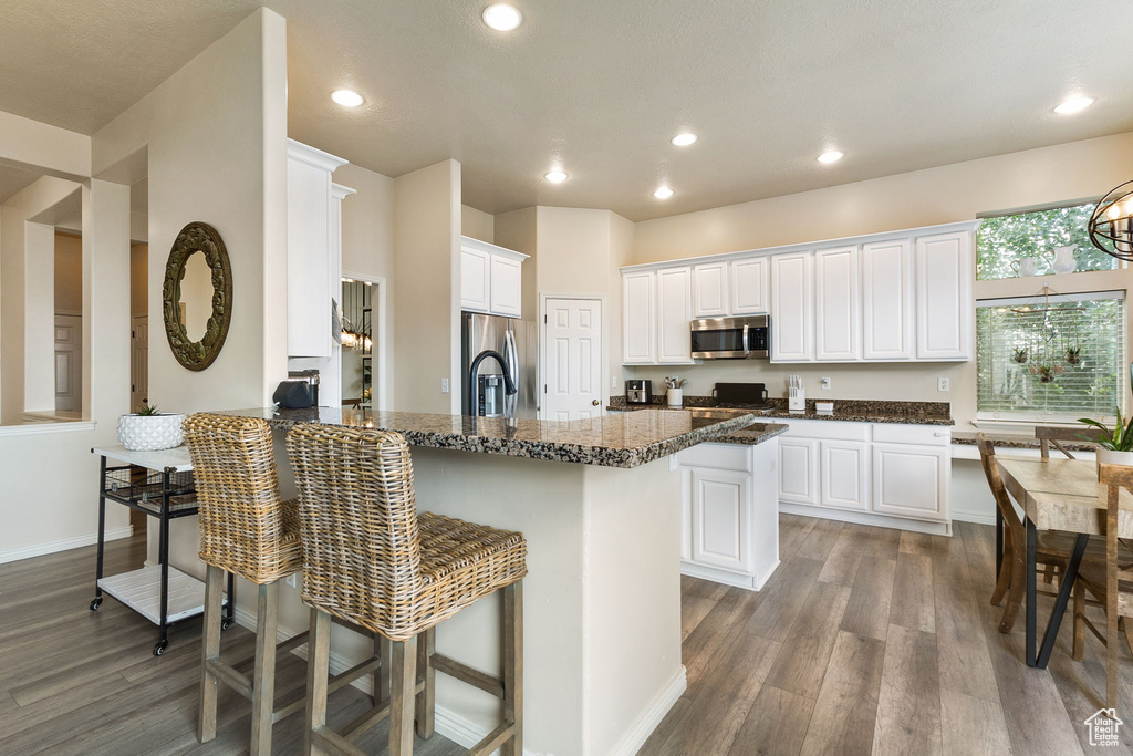 Kitchen with stainless steel appliances, wood finished floors, a kitchen breakfast bar, a peninsula, and recessed lighting