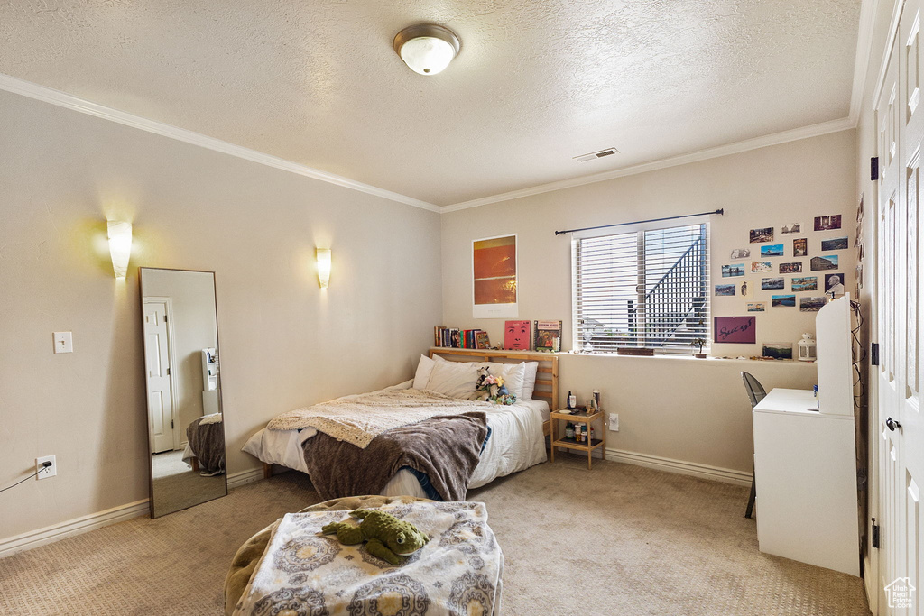 Bedroom featuring light colored carpet, ornamental molding, and a textured ceiling
