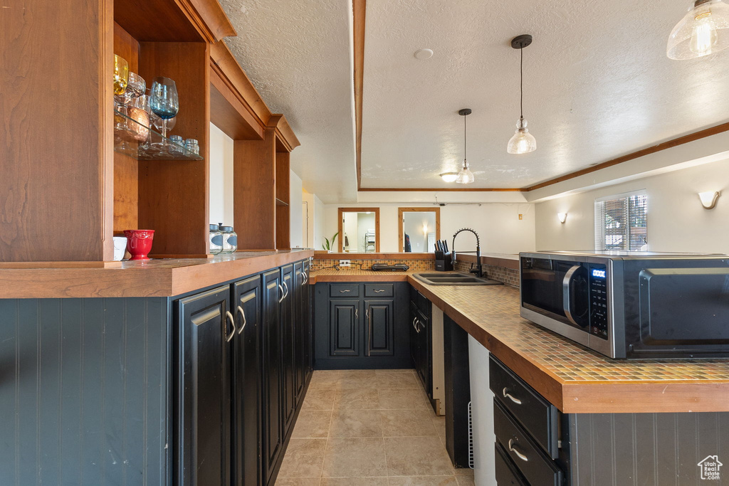 Kitchen with stainless steel microwave, a peninsula, wooden counters, light tile patterned flooring, and decorative light fixtures