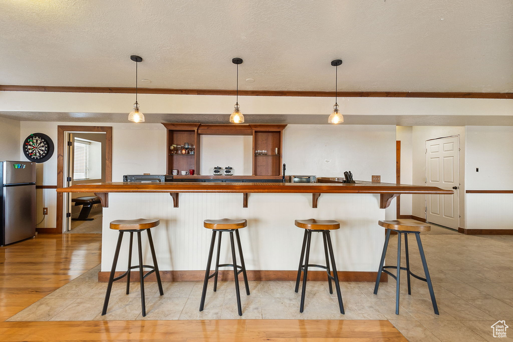Kitchen featuring freestanding refrigerator, a kitchen bar, pendant lighting, wooden counters, and a textured ceiling