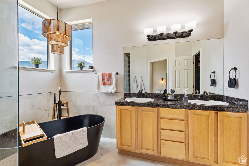 Full bathroom with tile walls, a freestanding tub, double vanity, and a wainscoted wall