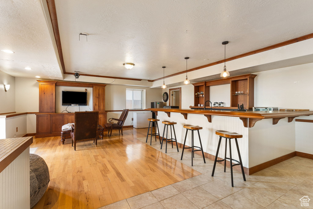 Kitchen with a textured ceiling, a breakfast bar area, a peninsula, brown cabinets, and crown molding