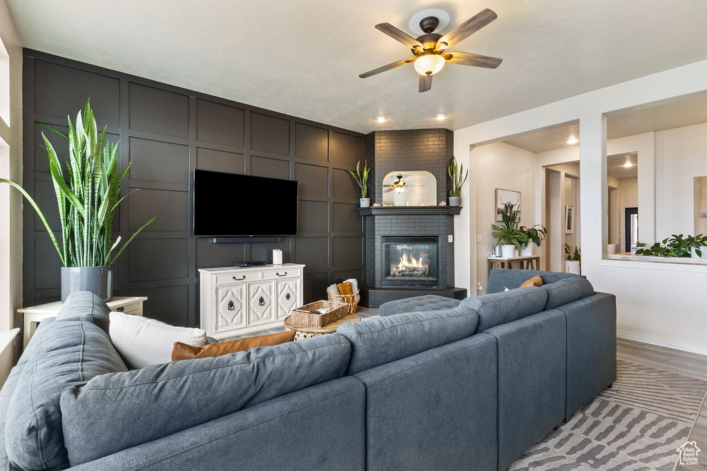 Living area featuring ceiling fan, a fireplace, light wood finished floors, and a decorative wall