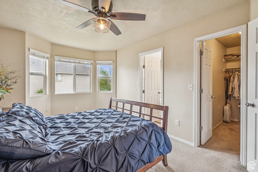 Bedroom with light carpet, a spacious closet, ceiling fan, and a textured ceiling