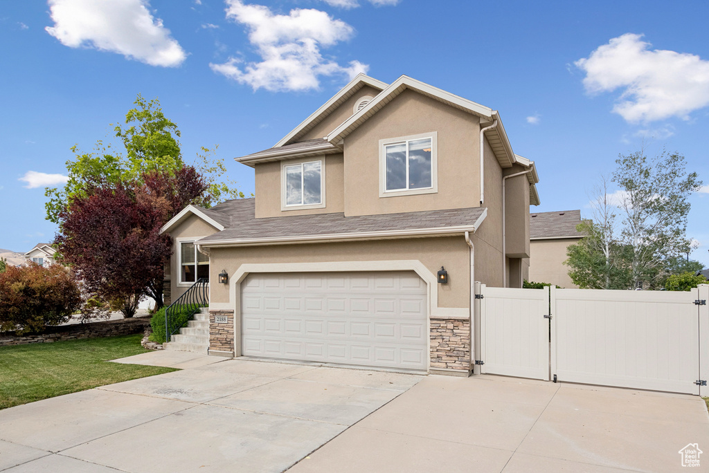 View of front of home with a gate, driveway, stucco siding, a garage, and stone siding