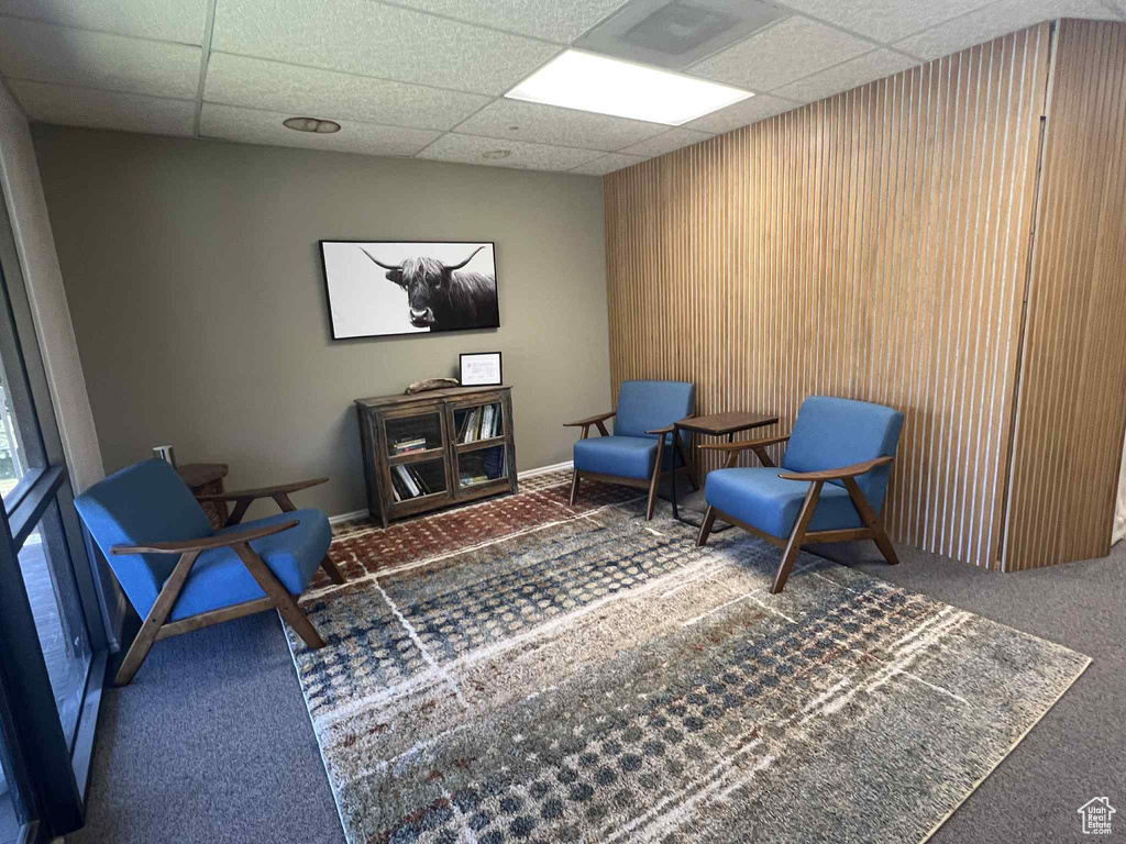Living area featuring carpet, a paneled ceiling, and wooden walls