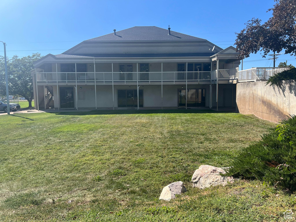Rear view of property with a lawn, stairs, roof with shingles, and a balcony