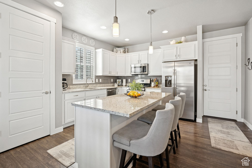 Kitchen featuring stainless steel appliances, white cabinets, dark wood-type flooring, a breakfast bar area, and recessed lighting