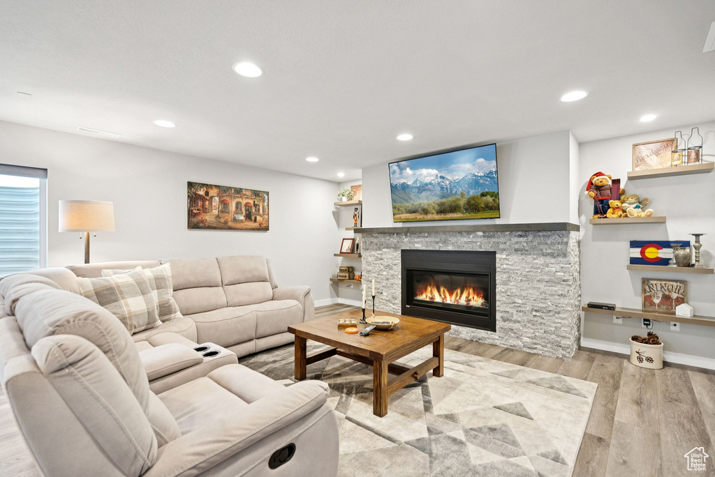 Living room with a stone fireplace, wood finished floors, and recessed lighting