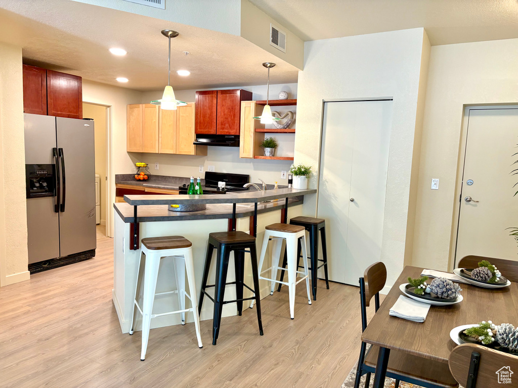 Kitchen featuring stainless steel fridge, under cabinet range hood, dark countertops, light wood-style floors, and a peninsula