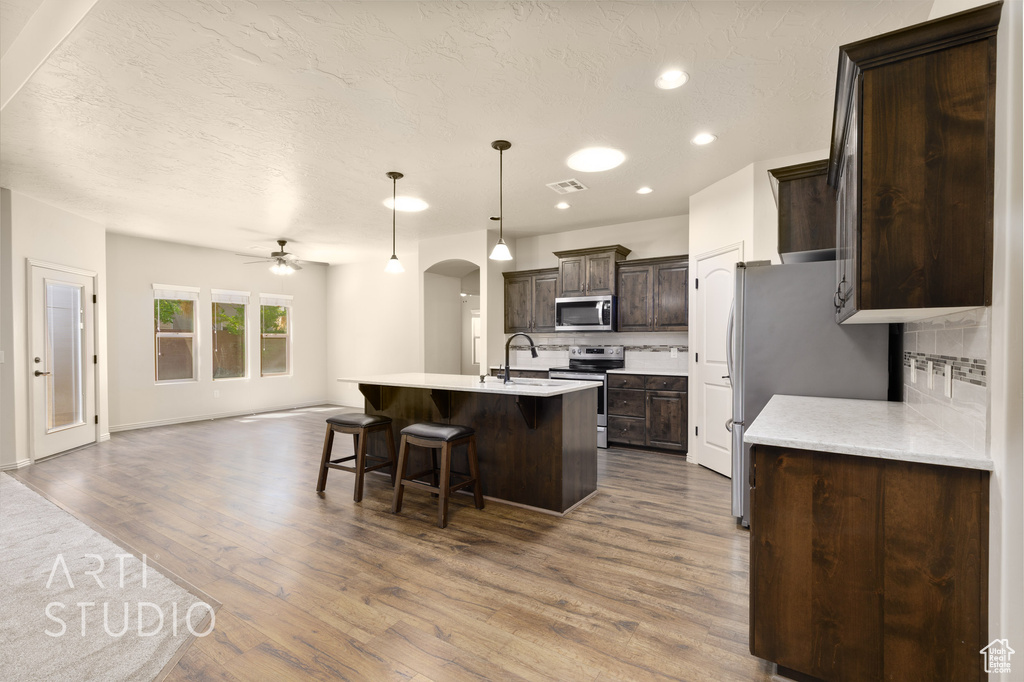 Kitchen with stainless steel appliances, open floor plan, dark brown cabinetry, decorative backsplash, and ceiling fan