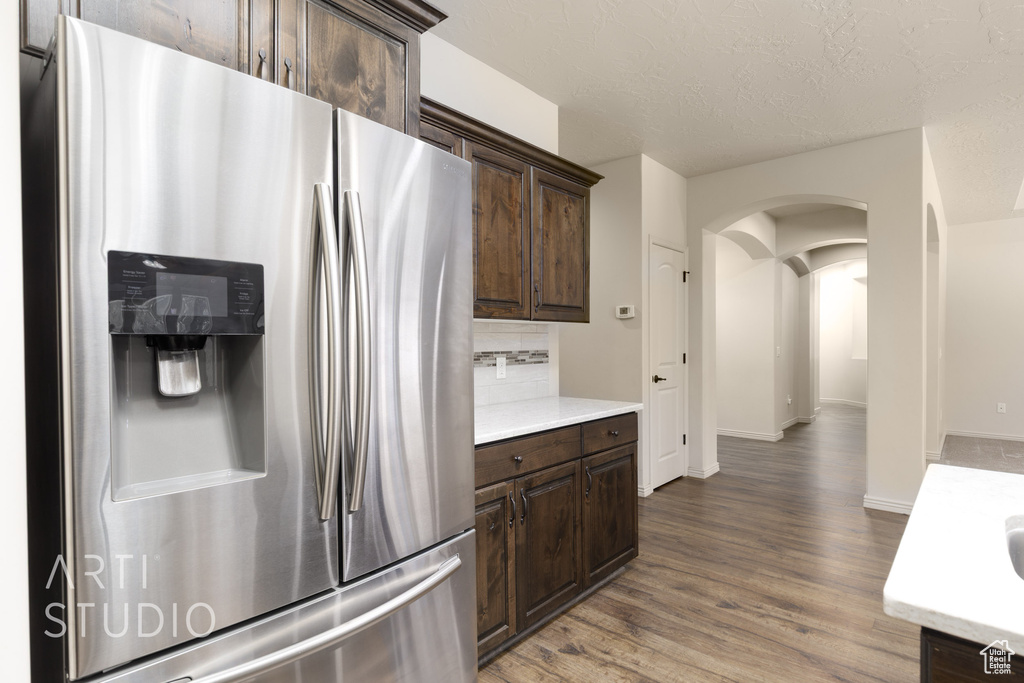Kitchen featuring stainless steel fridge with ice dispenser, arched walkways, dark brown cabinetry, and light countertops