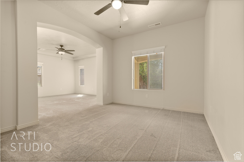 Spare room featuring ceiling fan, carpet floors, and arched walkways