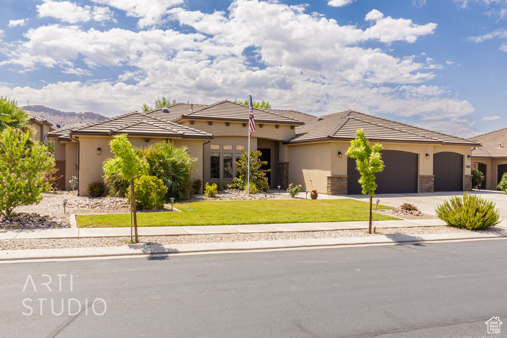 View of front facade with concrete driveway, a garage, a front lawn, stucco siding, and a tile roof