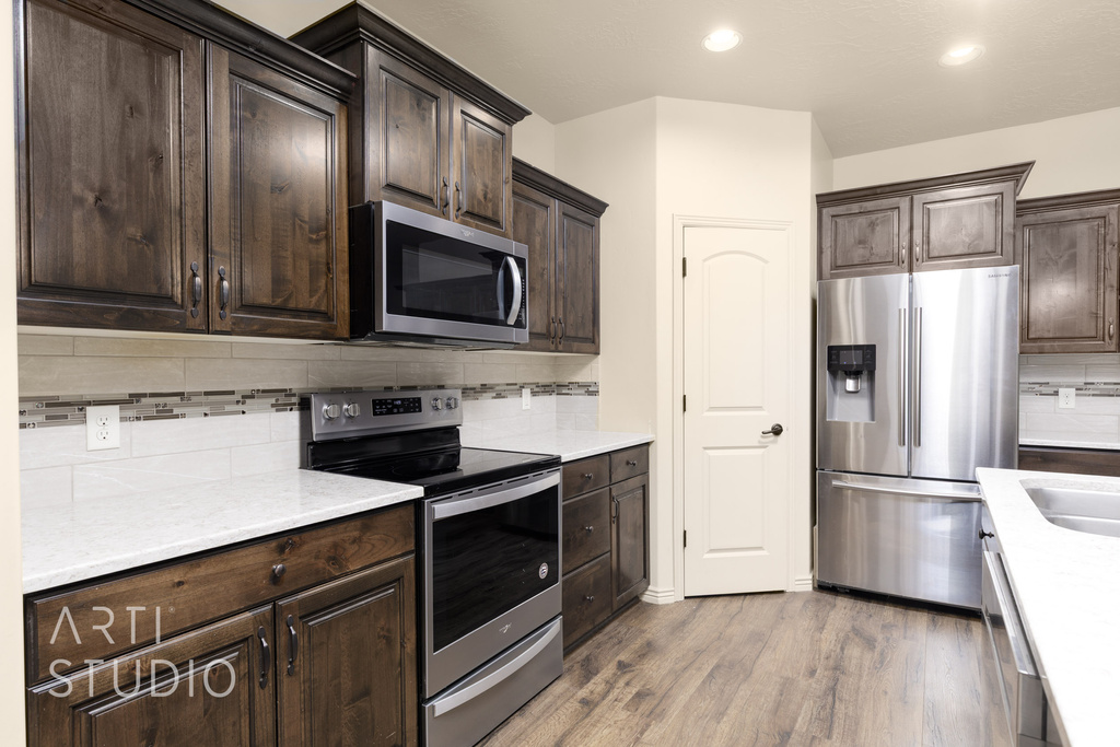 Kitchen with stainless steel appliances, dark brown cabinets, backsplash, wood finished floors, and light countertops