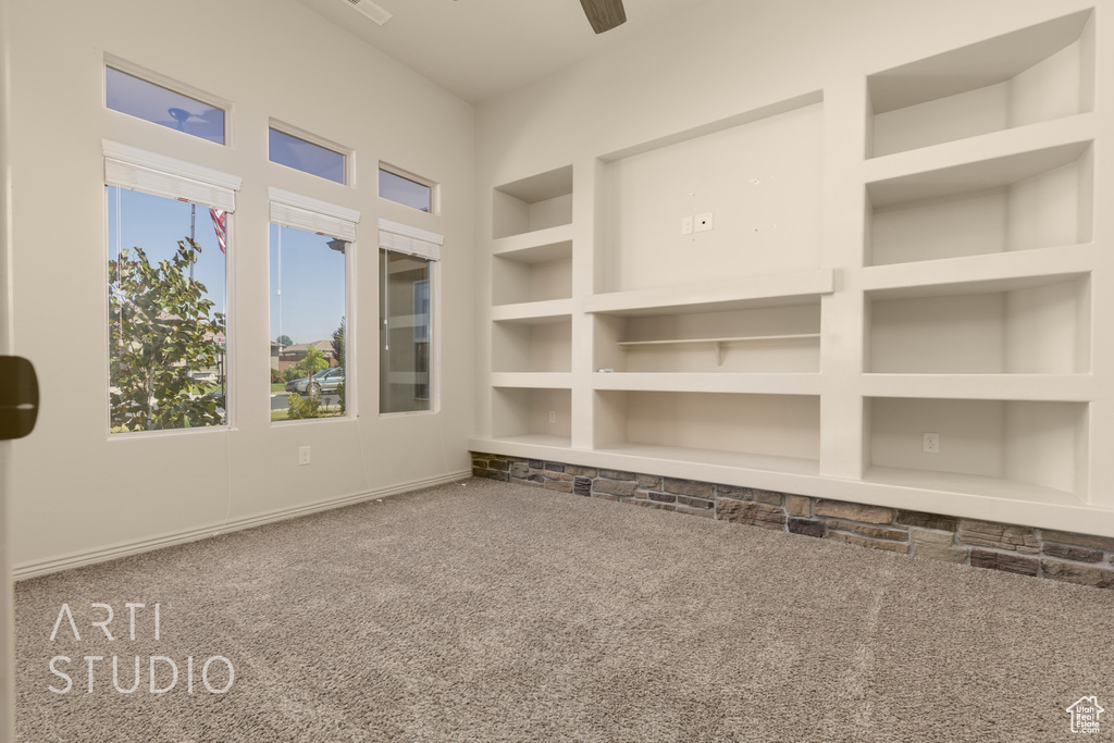 Empty room featuring carpet flooring, built in features, and ceiling fan