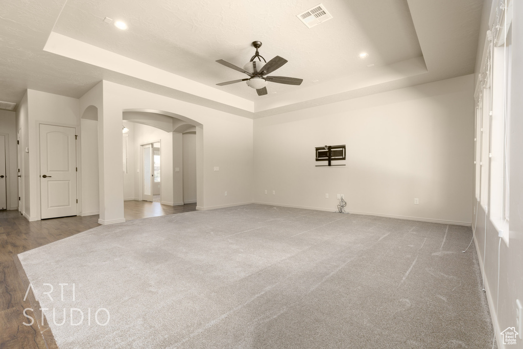 Unfurnished room featuring a tray ceiling, a ceiling fan, arched walkways, light colored carpet, and recessed lighting