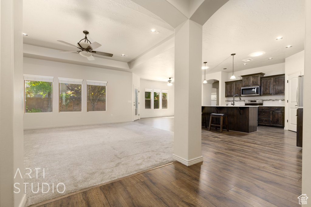 Unfurnished living room featuring ceiling fan, dark wood finished floors, recessed lighting, arched walkways, and a tray ceiling