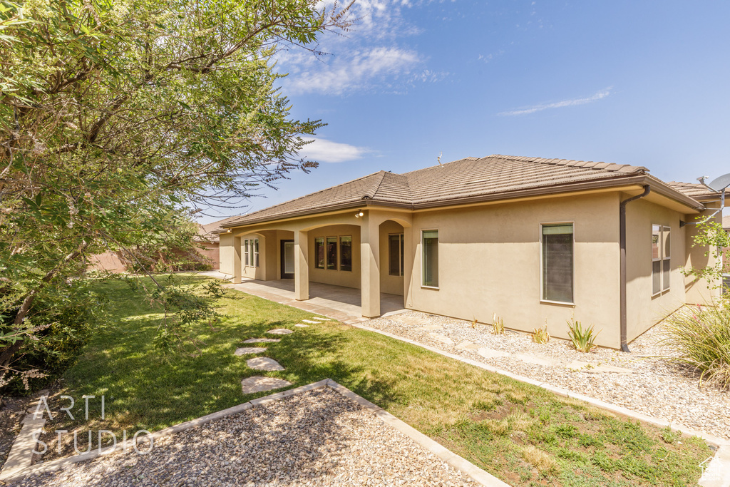 Rear view of property with stucco siding, a yard, a patio, and a tiled roof